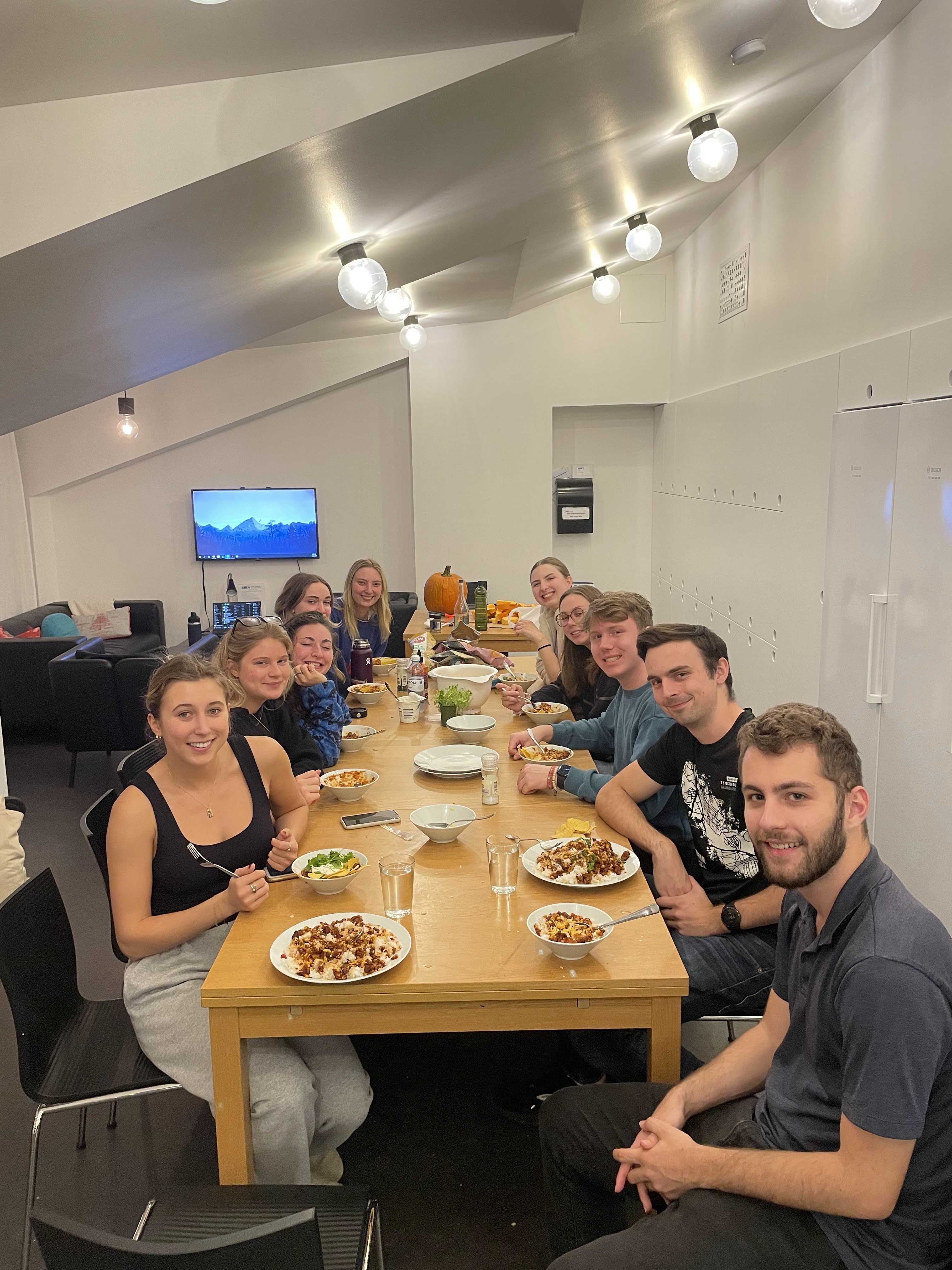 A group of students sit at a table with food and smile inside a DIS Residential Community.